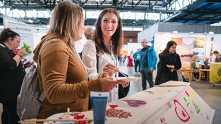 Frau, die Sarg bemalt, lächelt auf einer Messe in die Kamera