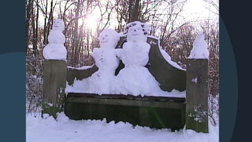 Schneemänner-Familie auf einer Bank im Bürgerpark