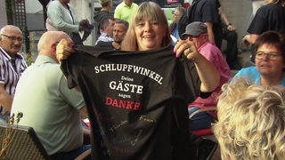 Ein Gast bei dem Schlupfwinkel Abschied mit einem T-Shirt, auf dem steht: "Schlupfwinkel, Deine Gäste sagen Danke!"