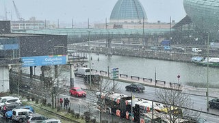 Auf einer nassen Straße fahren Autos im Schneegestöber.