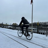 Ein Mann fährt auf Fahrrad bei Schnee an der Weser entlang 