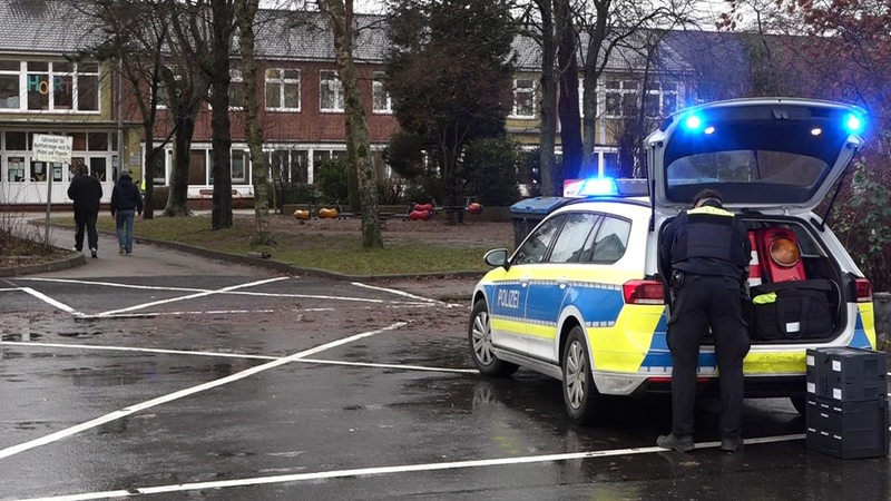 Ein Polizeiauto steht vor einem Schulgebäude.