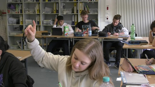 Eine Schülerin der 10. Klasse meldet sich. Hinter ihr sitzen andere Mitschüler in einer Reihe an ihren Tischen.