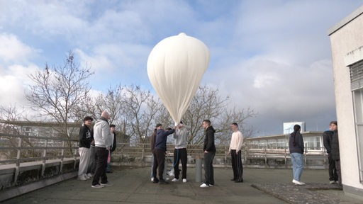 Schüler auf einem Schuldach lassen gemeinsam eine Stratosphäreballon steigen.