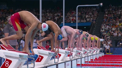 Eine Reihe Schwimmer stehen vor einem Wettkampf bei Olympia auf ihren Startblöcken.