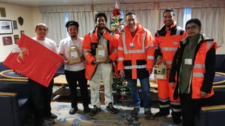 In der Bremerhavener Seemannsmission posieren mehrere Menschen vor einem Weihnachtsbaum für ein Erinnerungsfoto.