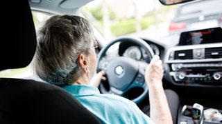 Eine über 90-jährige Frau sitzt hinter dem Lenkrad eines Autos..