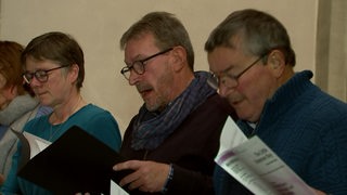 Mehrere Chorsänger singen und schauen in ihre Texte.