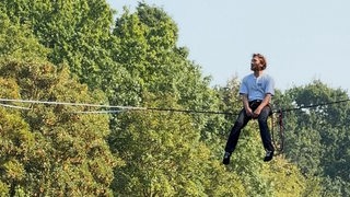 Ein Slackliner balanciert auf einem Seil über einen Fluss.