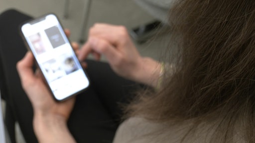 Eine Person mit einem Smartphone in der Hand. Der Seiteninhalt ist nicht zu erkennen.