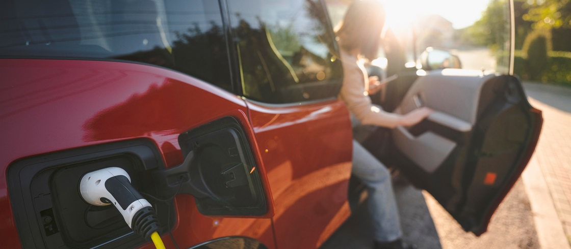 Eine Frau steigt bei sonnigen Wetter aus ihrem E-Auto aus, was gerade aufgeladen wird.