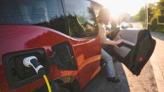 Eine Frau steigt bei sonnigen Wetter aus ihrem E-Auto aus, was gerade aufgeladen wird.