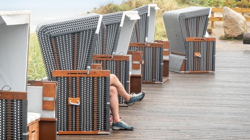 Ein Tourist sitzt bei Regenwetter an einer Strandpromenade in einem Standkorb