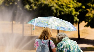 Zwei Frauen schützen sich mit einem Schirm vor der Sonne.