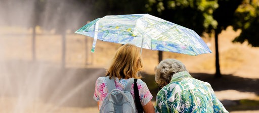 Zwei Frauen schützen sich mit einem Schirm vor der Sonne.