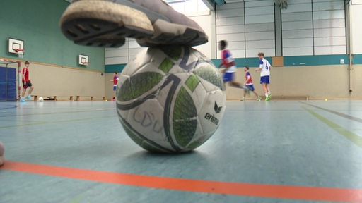 Ein Training in einer Sporthalle, ein Fußball im Vordergrund