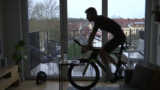 Eine Person fährt auf einem Trainingsfahrrad in einer Wohnung.