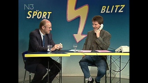 Willi Lemke und Ludwig Evertz unterhalten sich im Sportblitz. Ludwig Evertz hält dabei ein Telefon ans Ohr.