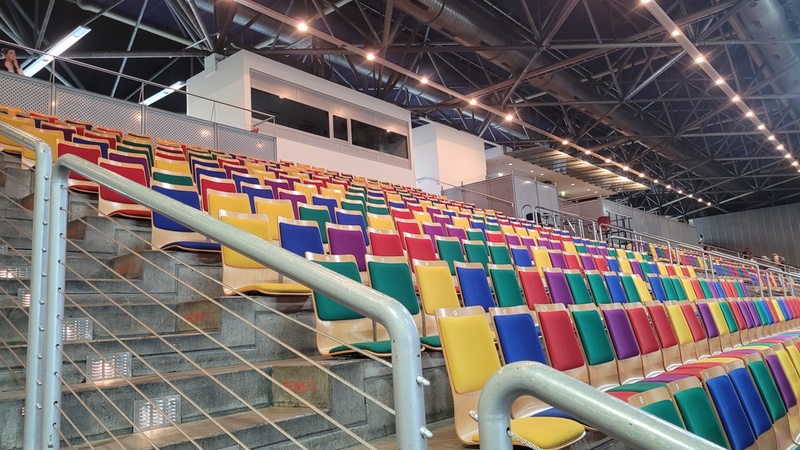 Blick auf eine Tribüne mit bunten Holzsitzen in einer Halle.