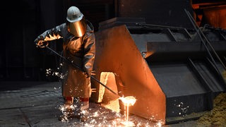 Ein Arbeiter in einem Stahlwerk nimmt an einem Hochofen eine Probe des flüssigen Roheisens. 