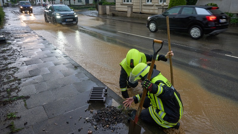 Nach unwetterartigen Regenfällen reinigen Feuerwehrleute Kanaldeckel. 