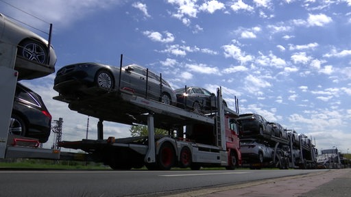 LKW´s stauen sich am rand einer Autobahn.Sie sind mit mit PKW´s beladen.