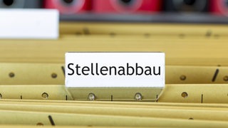 Auf einem Schild an einer Aktensammlung steht das Wort "Stellenabbau".