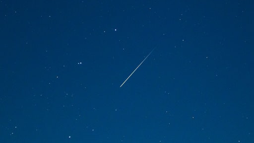 Eine Sternschnuppe leuchtet am Sternenhimmel.