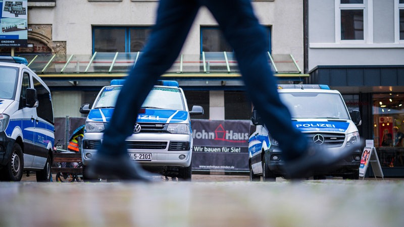 Ein Mensch läuft vor mehreren Polizeifahrzeugen lang.