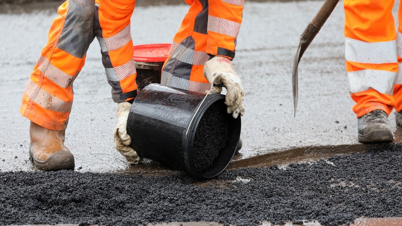 Ein Bauarbeiter schüttet Asphalt auf.