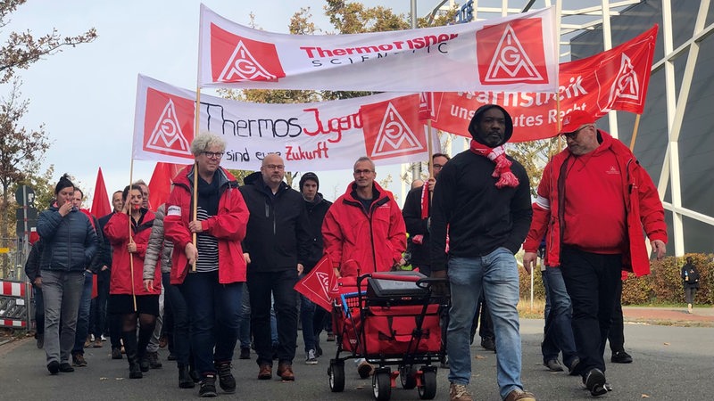 Bremer Beschäftigte von Thermo Fisher Scientific laufen demonstrierend über eine Straße.