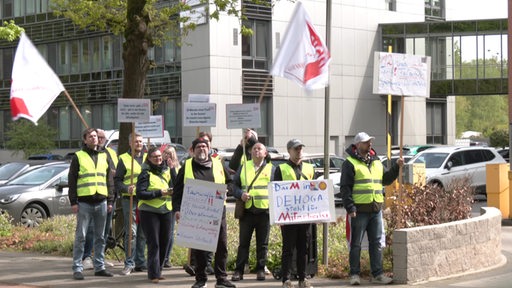 Streikende Menschen in Warnwesten halten Zahlreiche Schilder hoch und schwenken Fahnen.