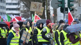 Menschen in gelben Warnwesten laufen in einem Demonstrationszug durch die Straßen und streiken.