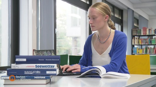 Die Nautik-Studentin Rayna Heupel sitzt vor vielen Büchern und ihrem Laptop.