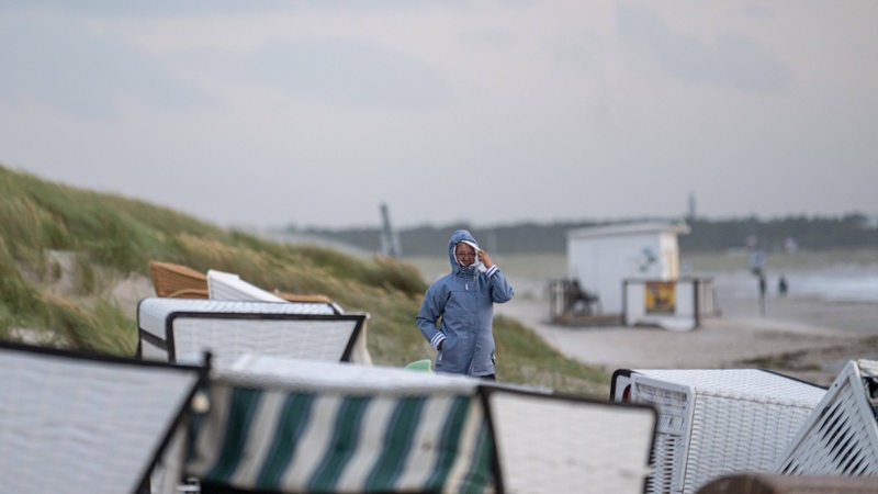 Eine Frau in Windjacke geht am Strand entlang.