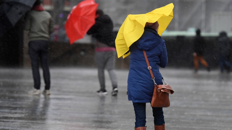 Passanten schützen sich mit Regenschirmen vor starkem Wind (Archivbild)