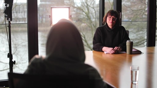 Ein verurteilter Straftäter sitzt mit dem Rücken zur Kamera im Interview mit Reporterin Johanne Bischoff.