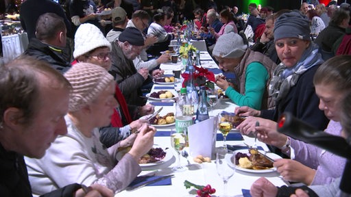 Bedürftige Menschen sitzen während eines Weihnachtsessens an einer langen Tafel