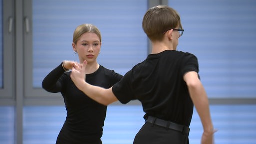 Eine junge Frau hält beim Tanzen einen jungen Mann an der Hand.