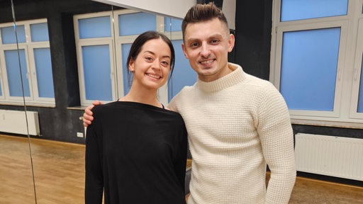 Das Tanzpaar des Bremer Grün-Gold-Clubs Malika Dzumaev und Zsolt Sandor Cseke stehen lächelnd Arm in Arm im Tanzsaal.