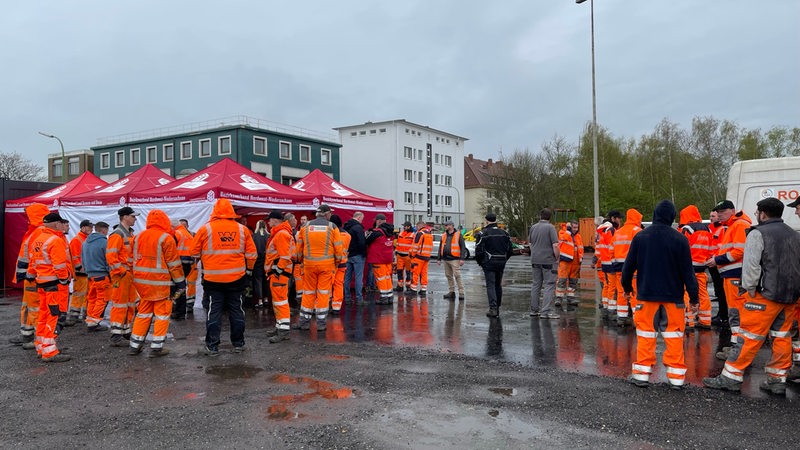 Eine Gruppe Bauarbeiter in oranger Kleidung steht auf einem Hof.