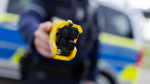 Ein Polizist hält einen Taser in Richtung Kamera.