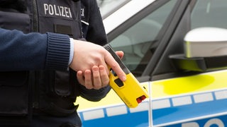 Ein Polizist hält einen gelben Taser in der Hand.