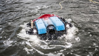 Ein rot-blaues Gerät mit einem Kabel daran schwimmt auf dem Meer.