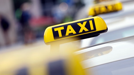 Taxi-Autos warten auf Fahrgäste. Zu sehen sind vor allem die Taxi-Schilder.