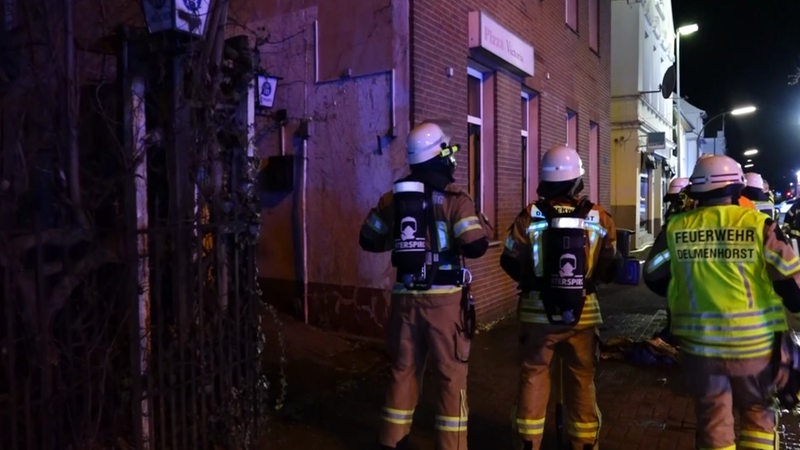 Feuerwehrleute stehen nach einem Brand vor einem Haus.