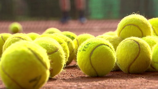 Tennisbälle liegen auf einem Sandplatz.