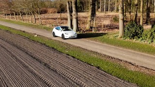 Ein weißer Tesla fährt einen Feldweg entlang