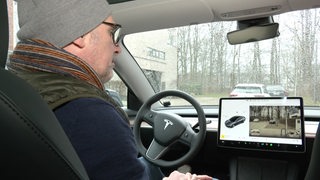 Zu sehen ist der Besitzer eines Teslas im Innenraum seines Fahrzeugs.