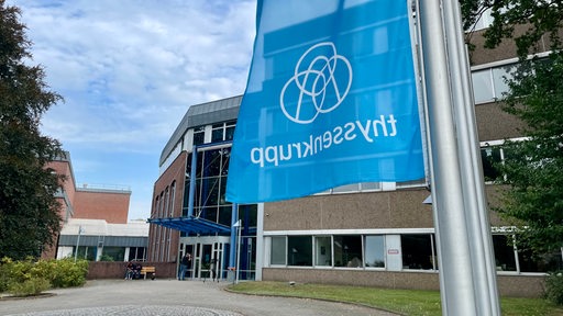 ThyssenKrupp-Gelände in Bremen-Nord, im Vordergrund eine Fahne des Konzerns, auf der das Logo zu sehen ist.